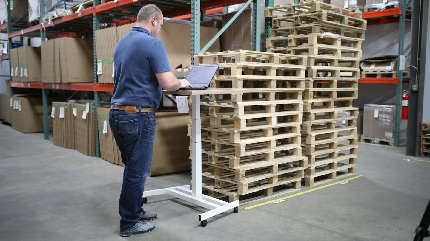 Man works on laptop at standing desk in warehouse.
